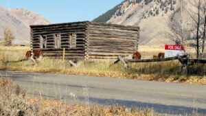 “Old wooden cabin for sale in Wyoming countryside with mountains in the background, symbolizing affordable marketing for small businesses during tough times.”