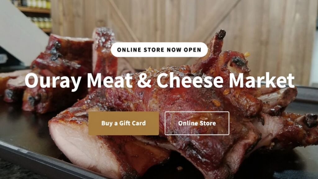 Close-up of smoked barbecue ribs and meats on display at Ouray Meat & Cheese Market, with "Buy a Gift Card" and "Online Store" buttons overlaid.