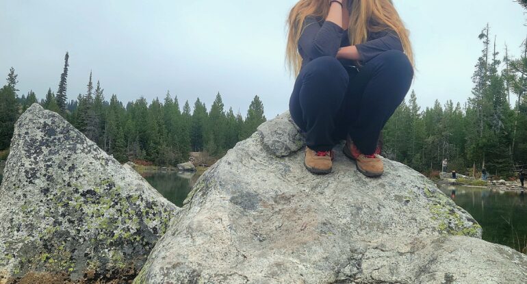 Faith sits on a rock by a lake in Grand Teton National Park